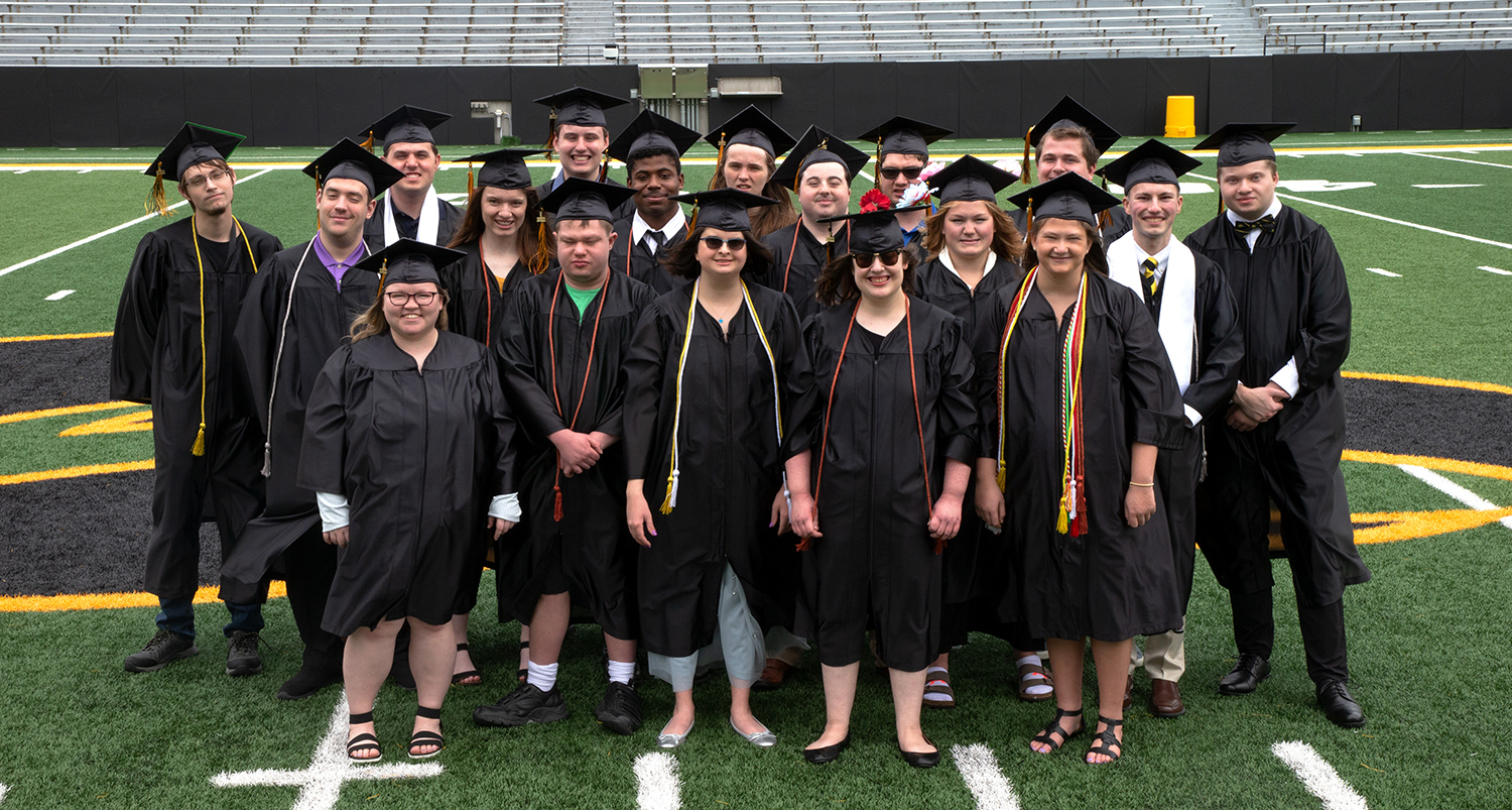 Group of students wearing graduation gowns standing on a football field