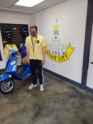 Person standing next to a scooter in a showroom.
