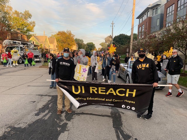 Students standing on a street, holding a UI REACH parade banner.