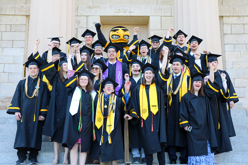 UI REACH 2024 graduates stand together in their caps and gowns.