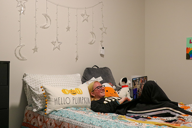 A UI REACH student lies on her bed at Aspire, working on her laptop.