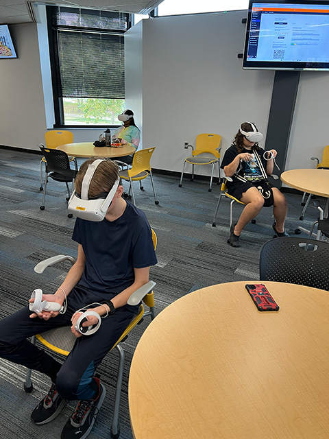Students sit in a room wearing virtual reality glasses.
