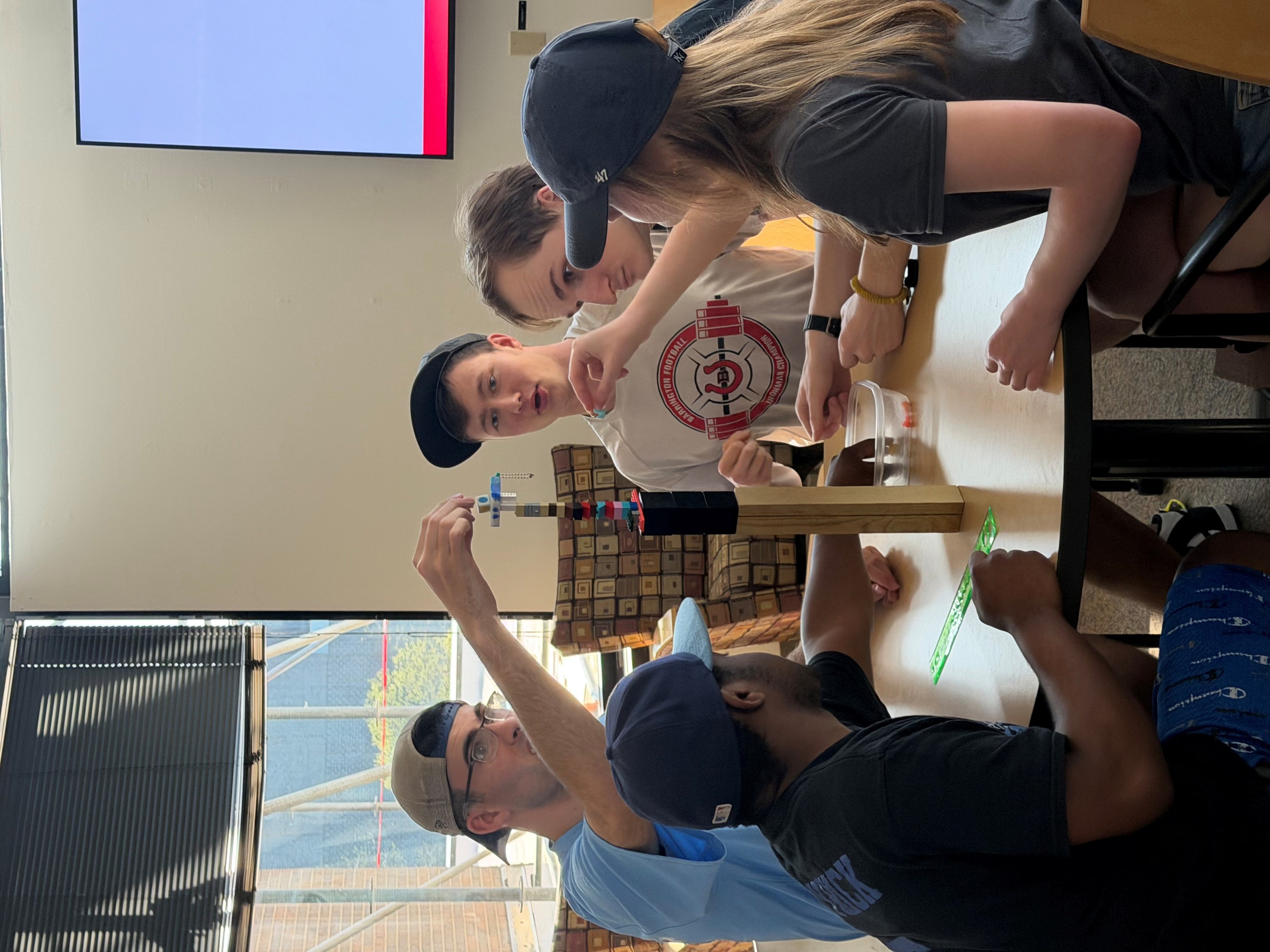 Students sit around a table, constructing a tower of blocks.