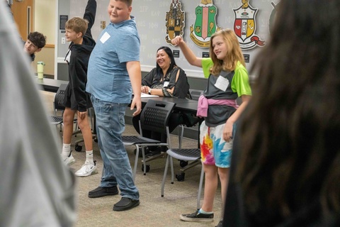 teacher smiles while watching students participate in group activity