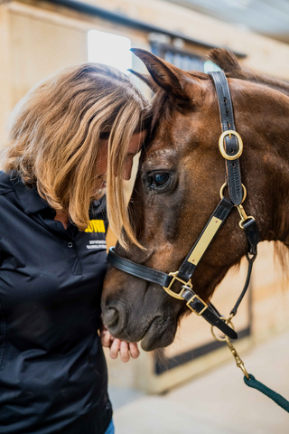 woman stands, leaning head towards horse's head