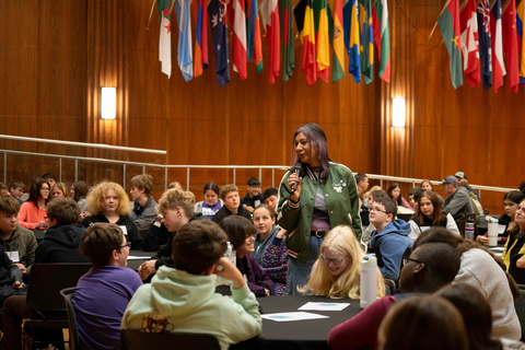 Woman stands in middle of crowded ballroom with microphone and smiles