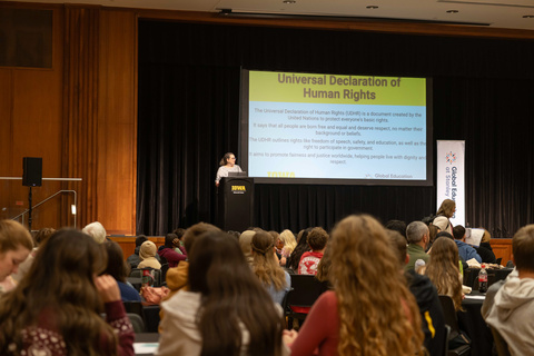Woman stands on stage in front of crowd of school-aged students