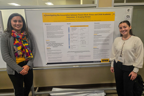 Duhita Mahatmya and Lucy Blissenbach stand smiling on either side of a research poster titled "Investigating the Association between Parent Work Stress and Child Academic Outcomes: A Scoping Review