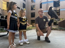 Man crouches while holding Hawk with two little girls standing near by