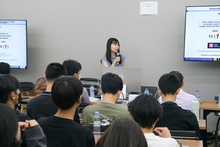 Lisa Nakahara stands in front of a room of students and speaks into a microphone