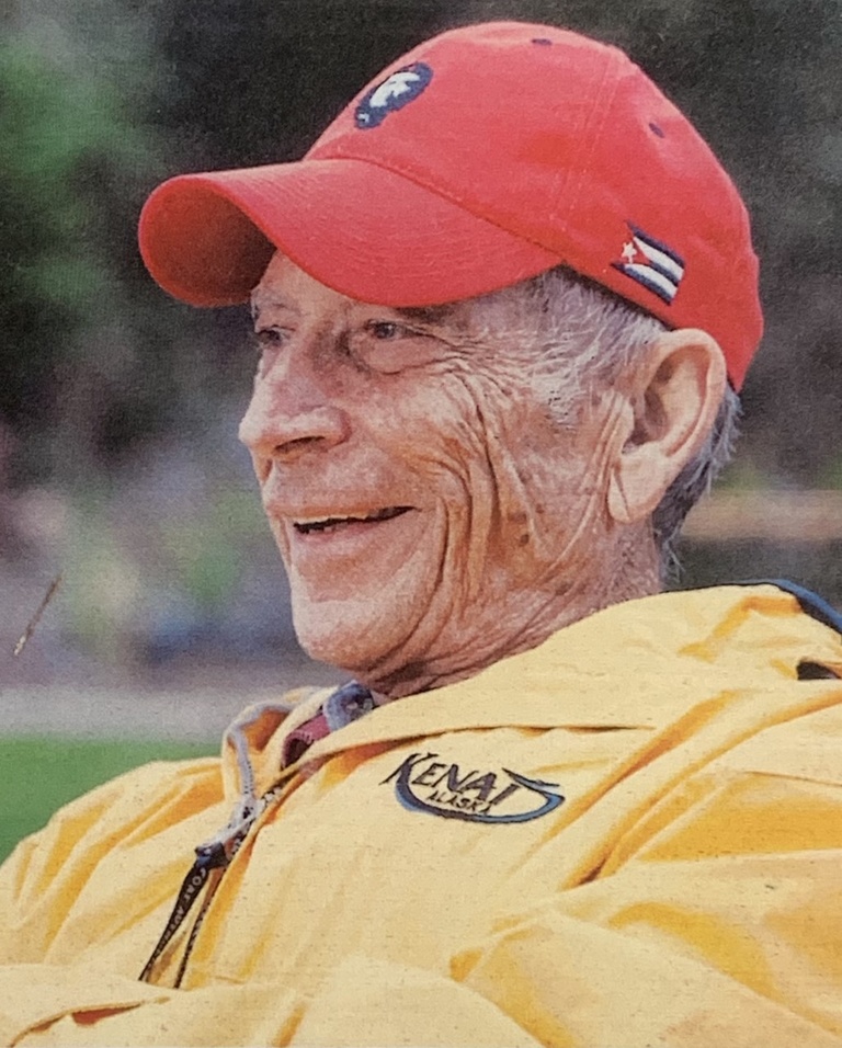 Older man smiles in cap and jacket outside