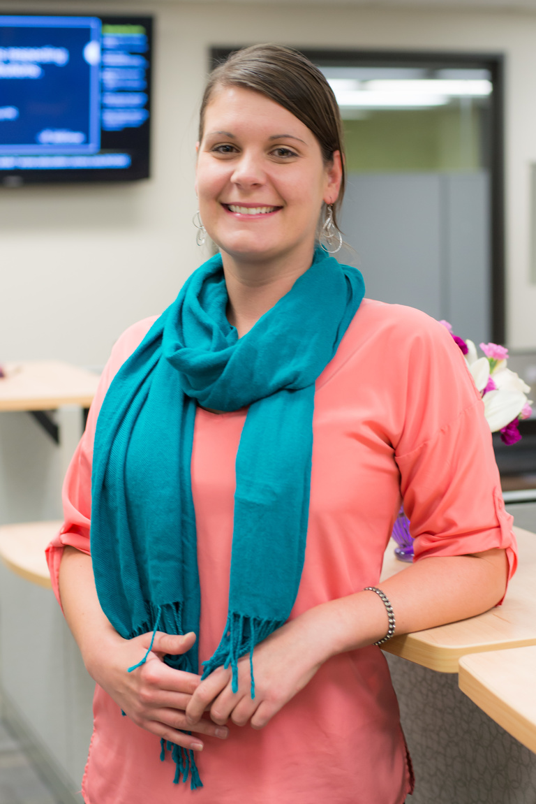 Headshot of alumna Ashley Rila wearing a teal scarf and peach button up shirt.