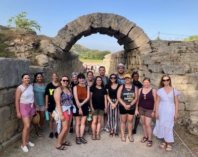Students and professor smile in front of archway in Greece