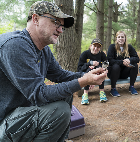 Dave Conrads holds a black-capped chickadee during a real-world bird-banding experience for future teachers.