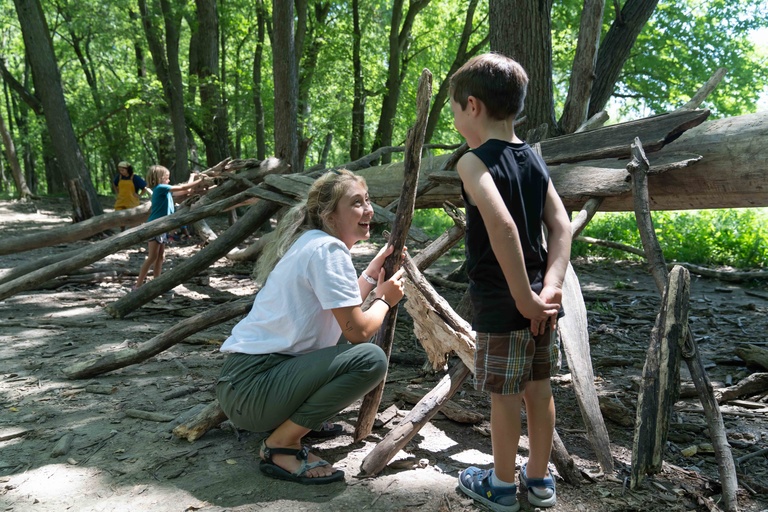 Children build a fort out of sticks in the woods. 