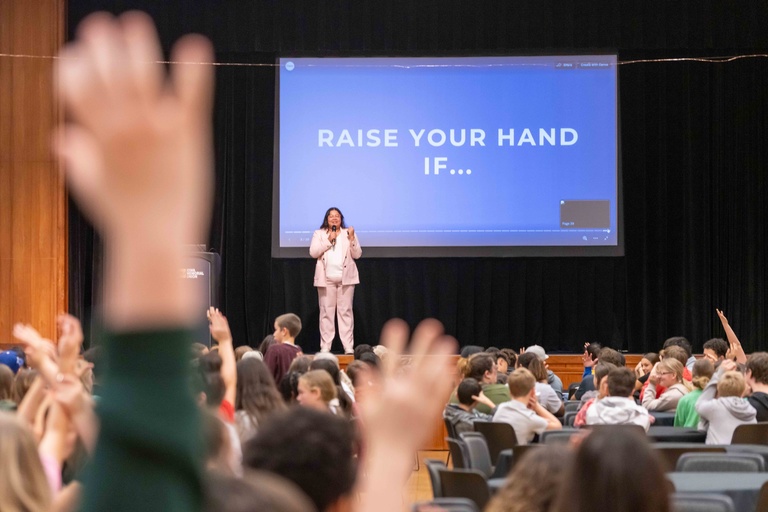 Woman stands in front of large crowd with hands raised