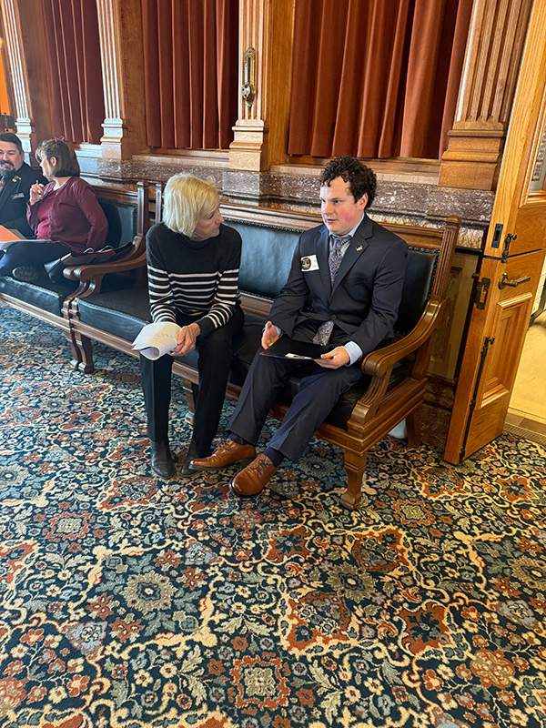 A UI REACH student and a state representative sit together on a bench, talking.