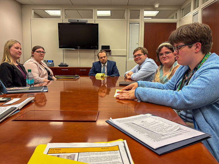 Students and staff members talk to each other at a conference table.