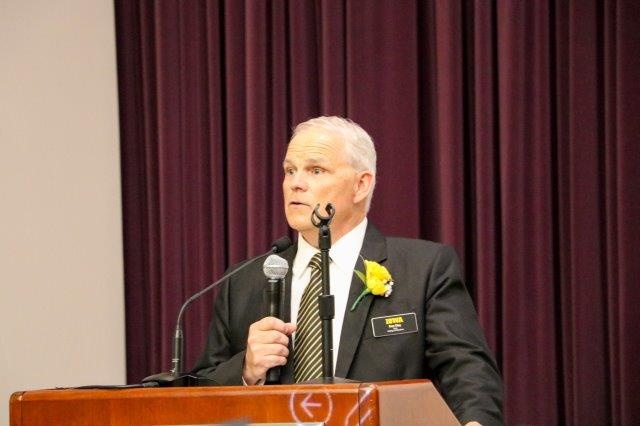 Dan Clay stands at a podium, holding a microphone.