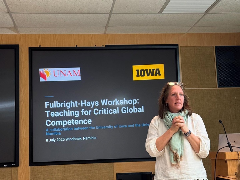 Woman stands in front of screen, lecturing