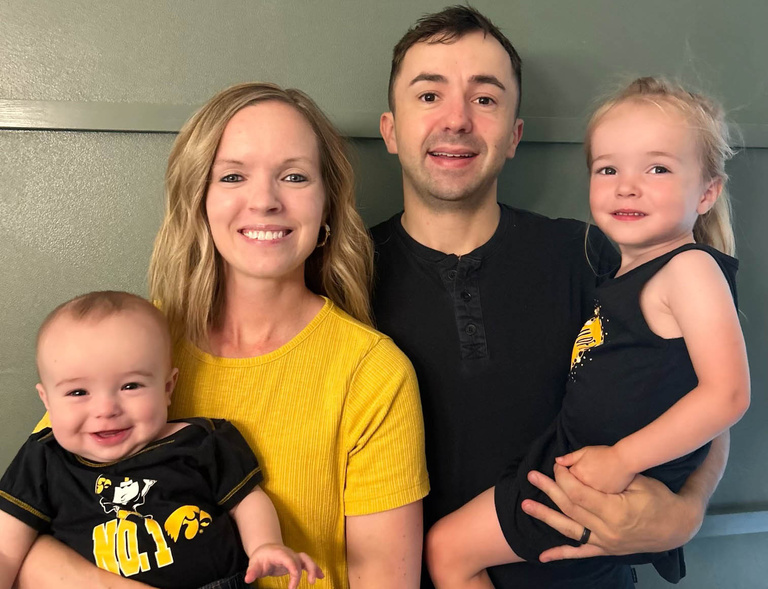 Christin Ferrall, her husband, and two children pose for a family photo wearing black and gold Hawkeye clothing.