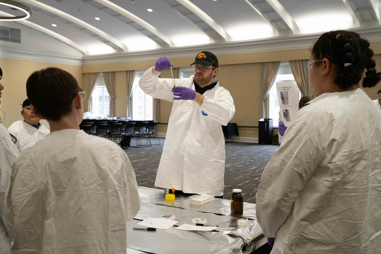 Man in lab coat uses dropper for experiment, showing students