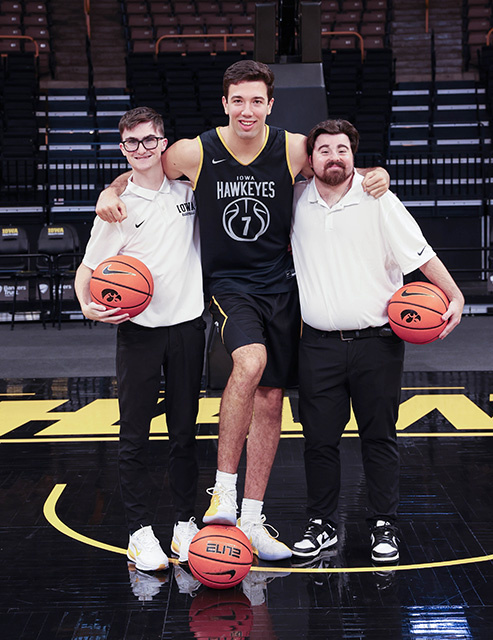 A UI REACH student and alum stand with a basketball player.