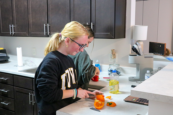 A student stands in her apartment kitchen, cooking.