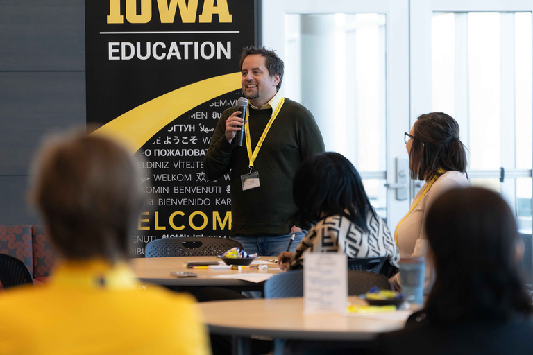 Professor Sam Tanner speaks in front of conference participants, holding a microphone.