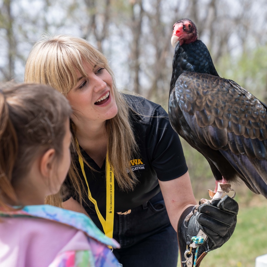 Woman holds a live turkey vulture and shows it to young girl