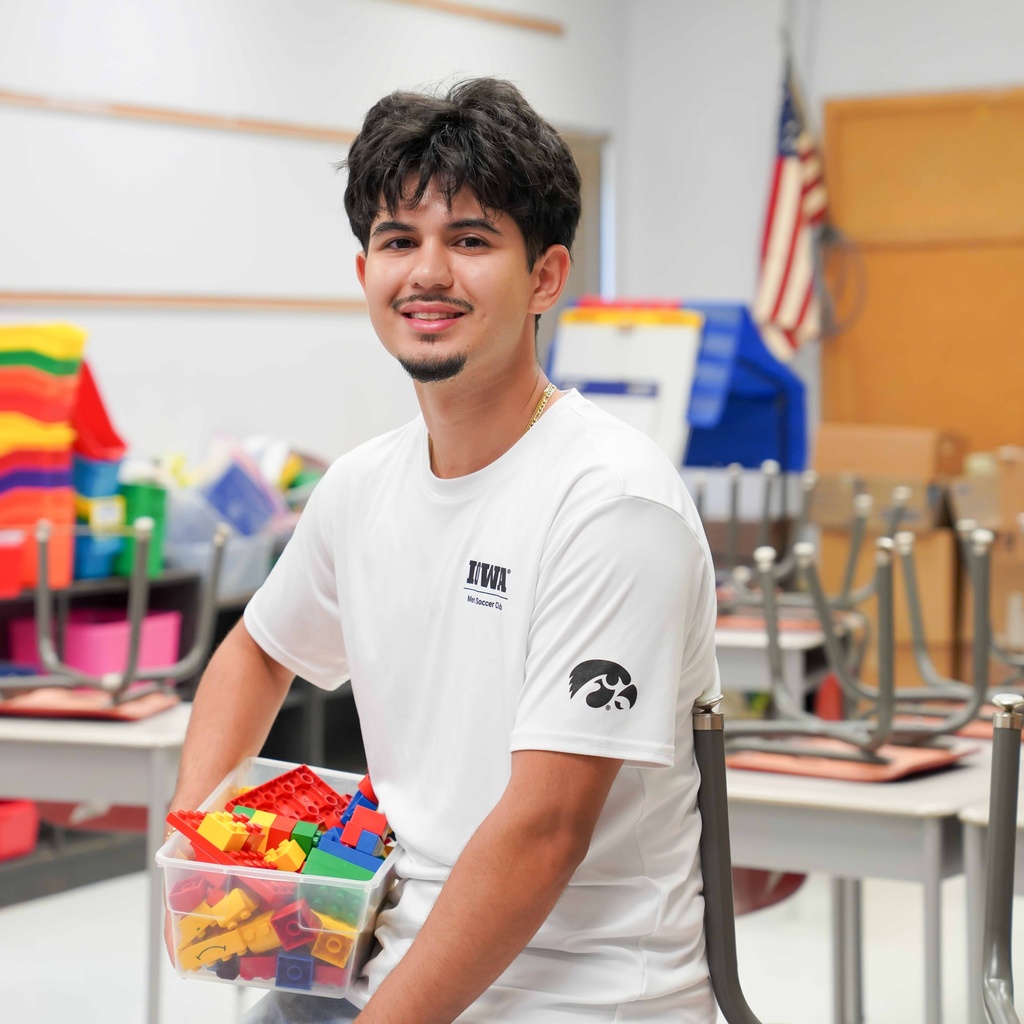 A male student holds a box of legos in his elementary school classroom.