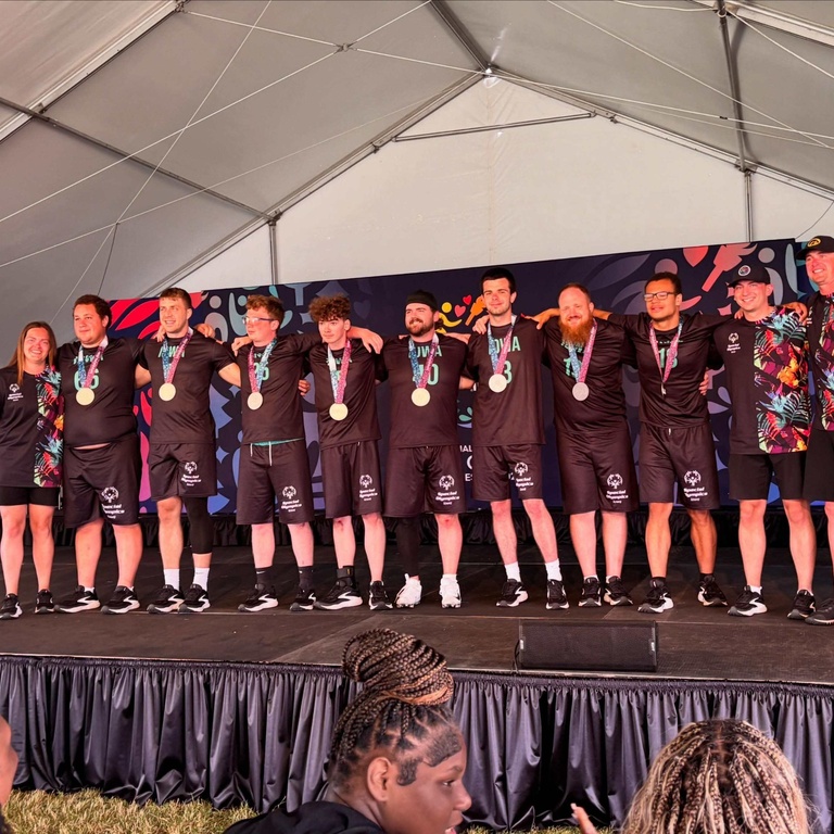 The flag football team stands together on stage, wearing silver medals.