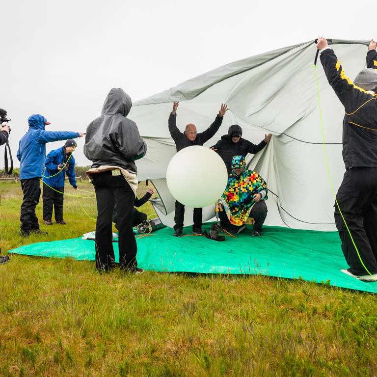 A group of faculty and students, outside, filling the balloon with helium. 