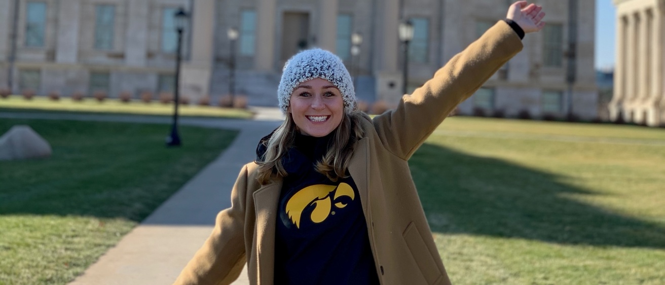 Hannah Baysinger poses with her arms extended outside of Old Capitol building