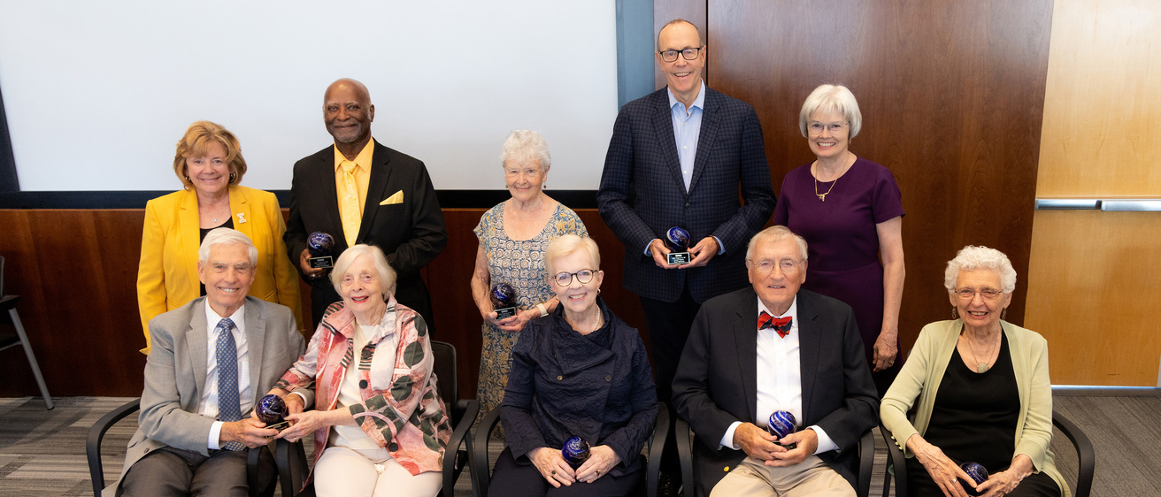 A group photo of UI alumni over the age of 80 being honored, sitting in a row of chairs.