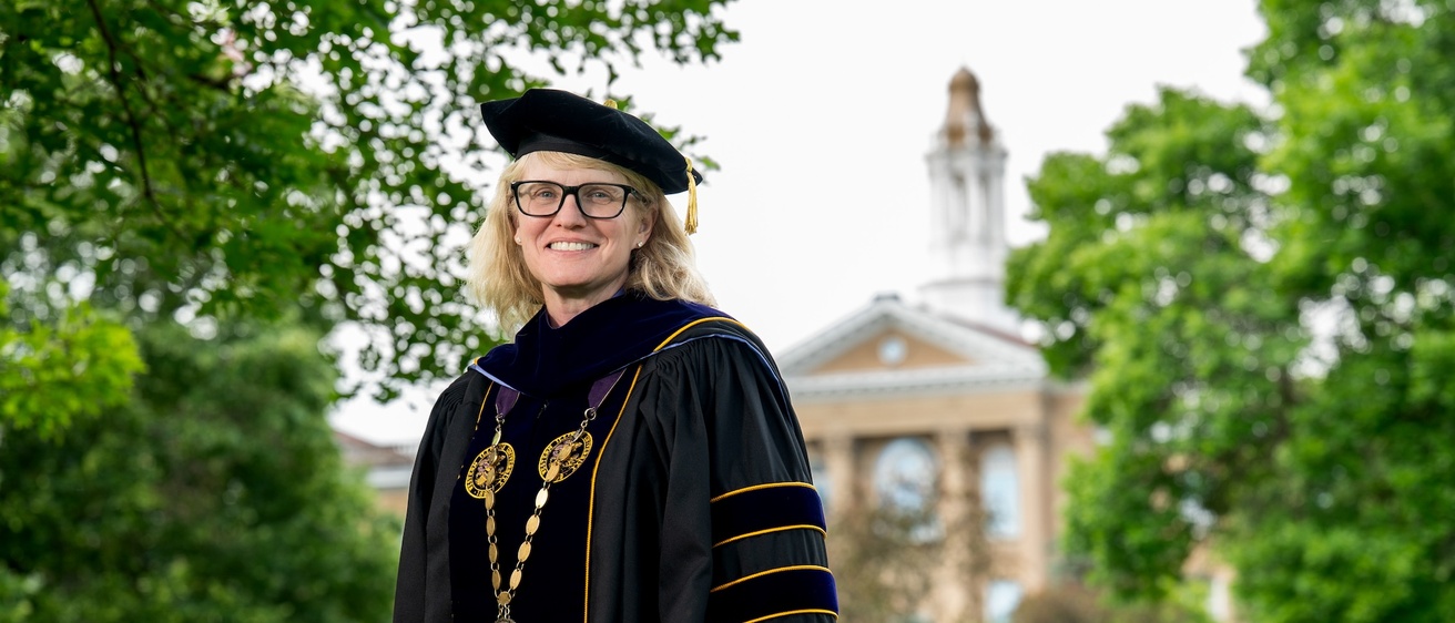 Woman in academic regalia smiles in front of building