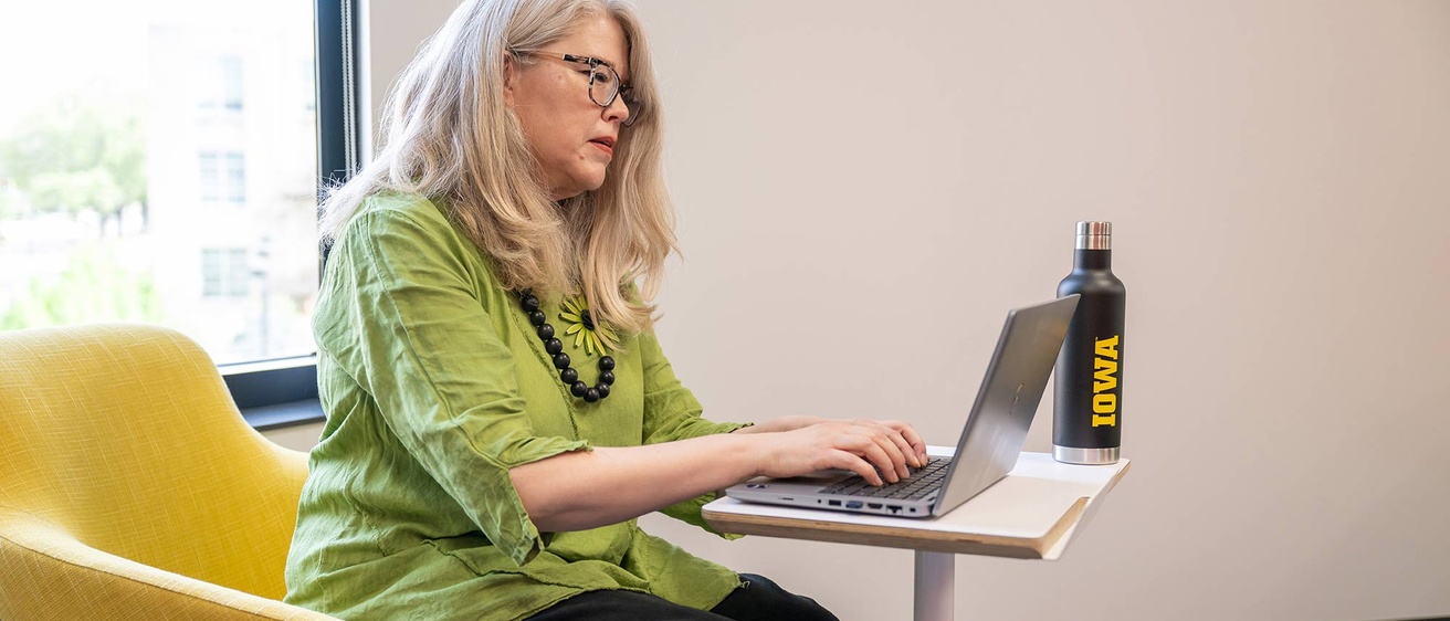 Staff member sits in front of a window working on her laptop. 