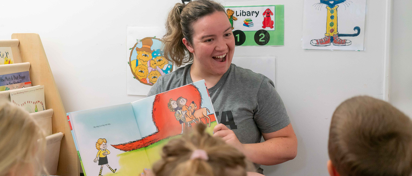 A UI REACH alumna reads the "Clifford The Big Red Dog" book to a group of pre-schoolers.