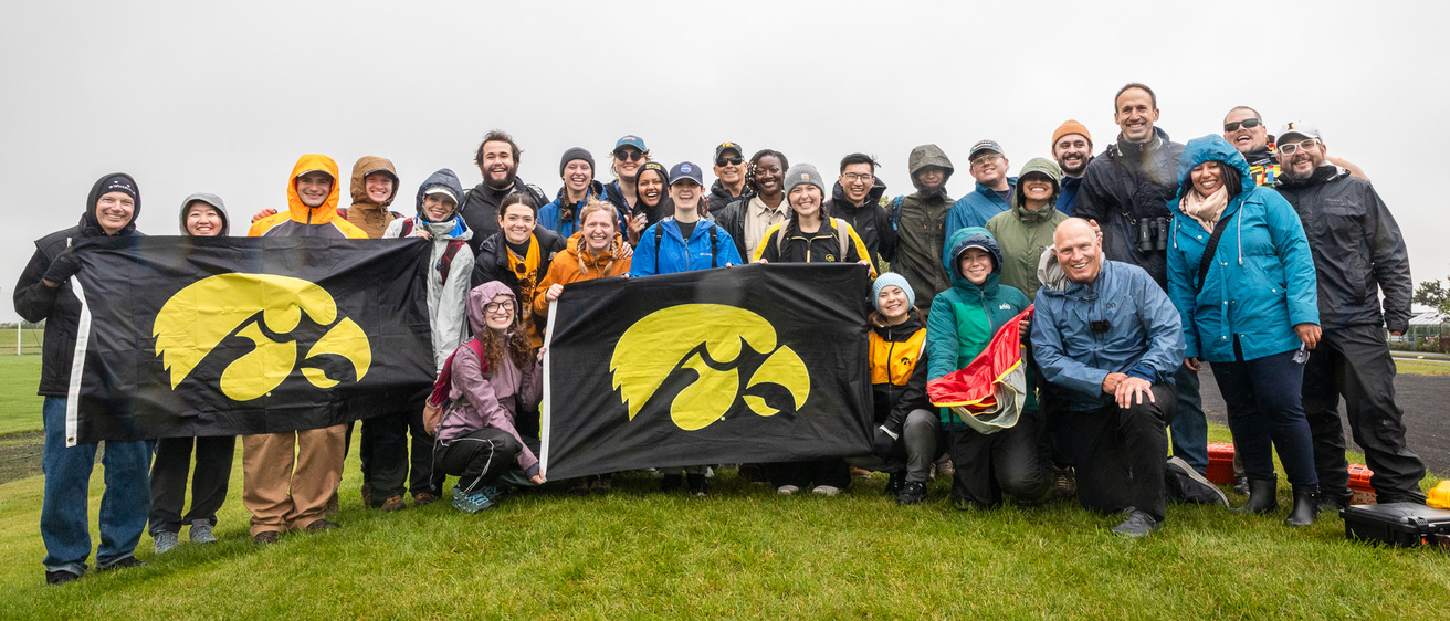 The entire interdisciplinary team, outside, smiling with Hawkeye flags after a successful launch.