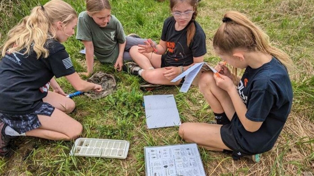 Kids outside sitting on the ground recording their findings during School of the Wild