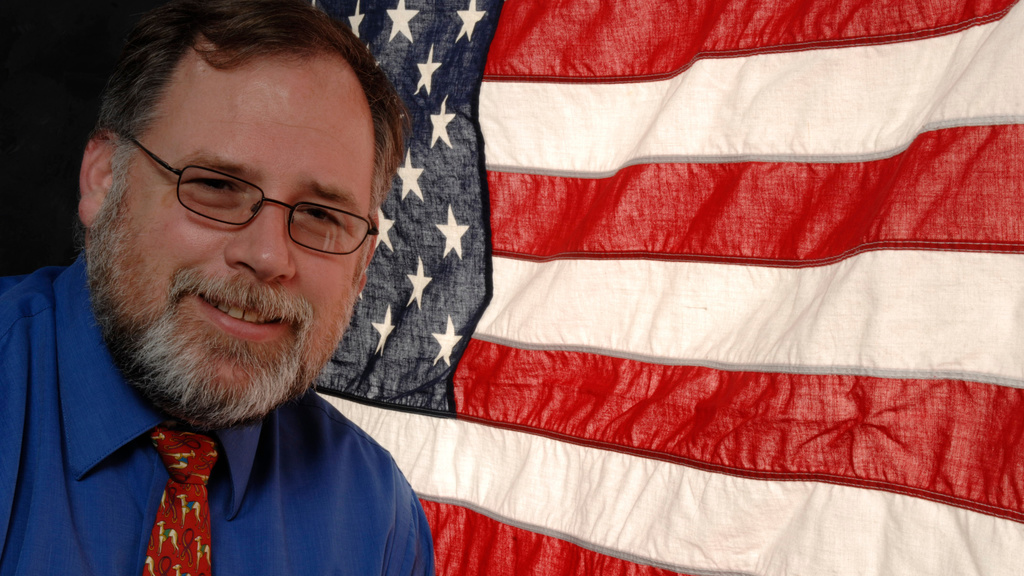 Alumna and veteran John Mikelson in front of a U.S. flag