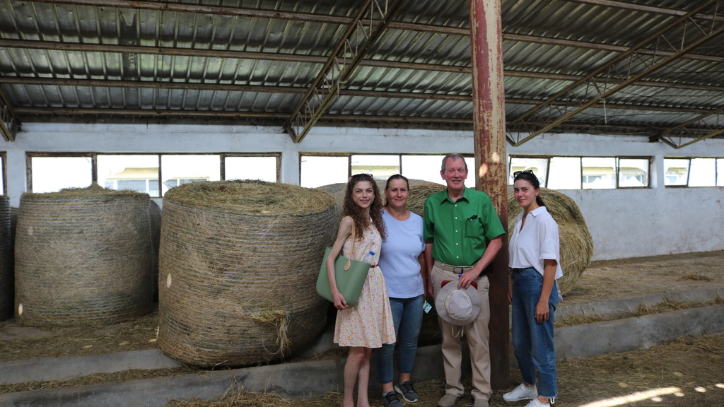 A group of people stand in front of hay bales during an agricultural tour in Kosovo.