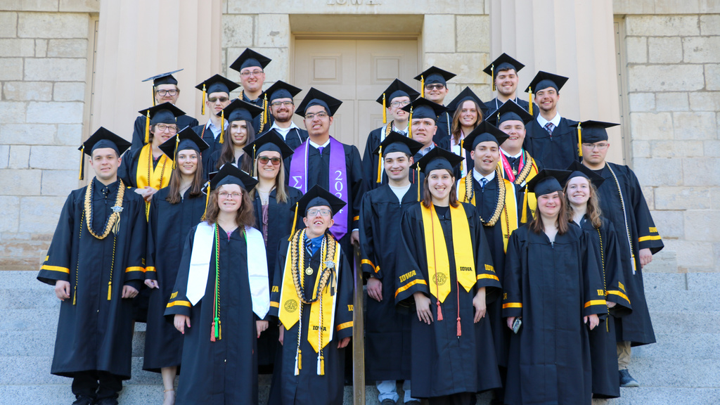 Students in cap in gown standing on steps of Old Capitol