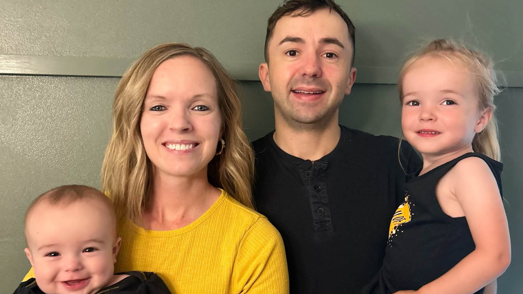 Christin Ferrall, her husband, and two children pose for a family photo wearing black and gold Hawkeye clothing.