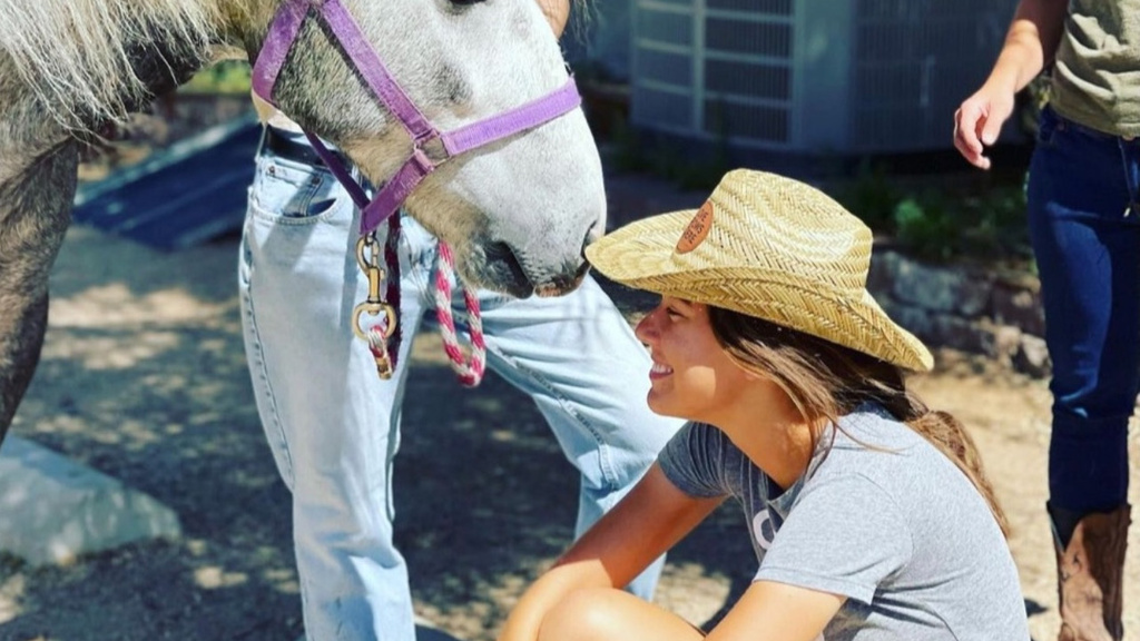 Woman crouches next to horse