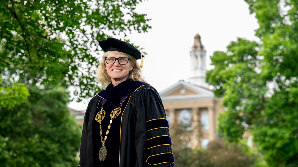 Woman in academic regalia smiles in front of building