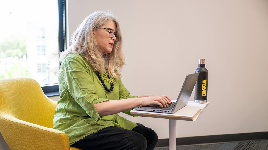 Staff member sits in front of a window working on her laptop. 