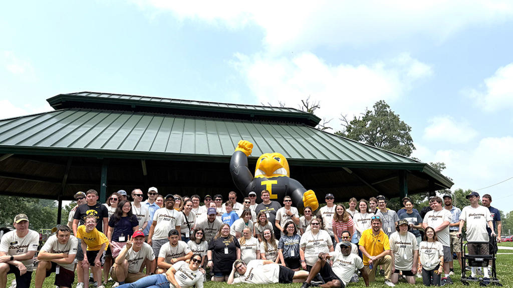 A large group of UI REACH community members gather around an inflatible Herky the Hawk.