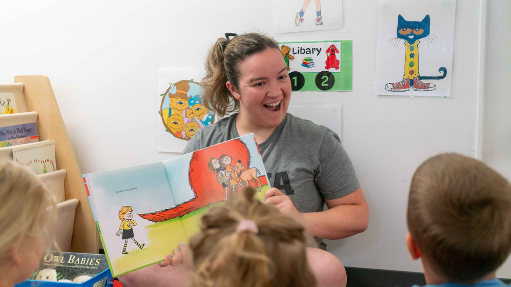 A UI REACH alumna reads the "Clifford The Big Red Dog" book to a group of pre-schoolers.