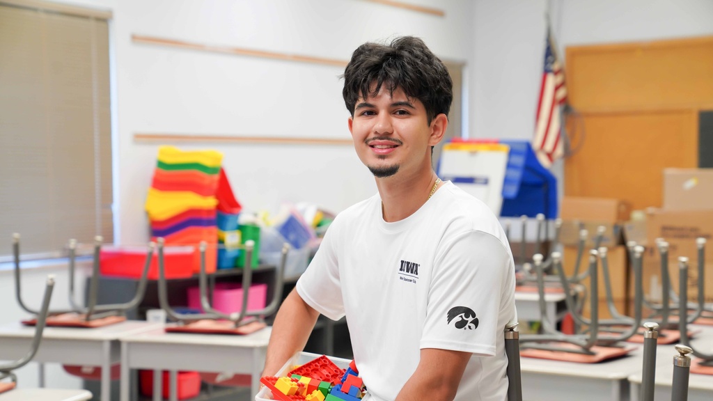 A male student holds a box of legos in his elementary school classroom.